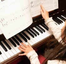 piano student girl plays piano pointing at lesson book